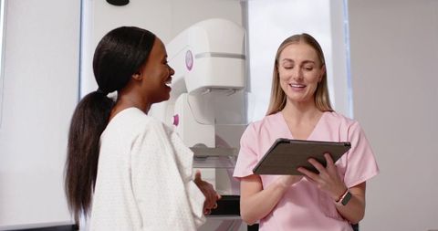 Radiology technologist reviewing tablet with patient preparing for mammogram in clinic