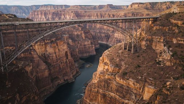 Steel-arch bridge spanning sandstone canyon over winding river with dramatic layered cliffs