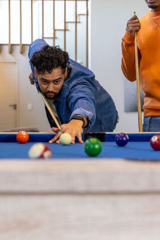 Friends playing pool at home lining up precise shot on blue felt billiard table