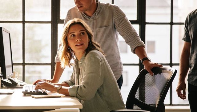 Young professional typing and turning toward colleague during collaborative office teamwork