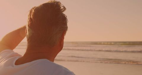 Senior Man Watching Sunset by Tranquil Beach Shore