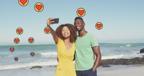 Couple taking selfie on beach with heart icons in background