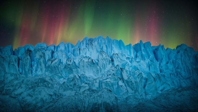 Jagged glacier ridge glowing under green and magenta aurora borealis at night