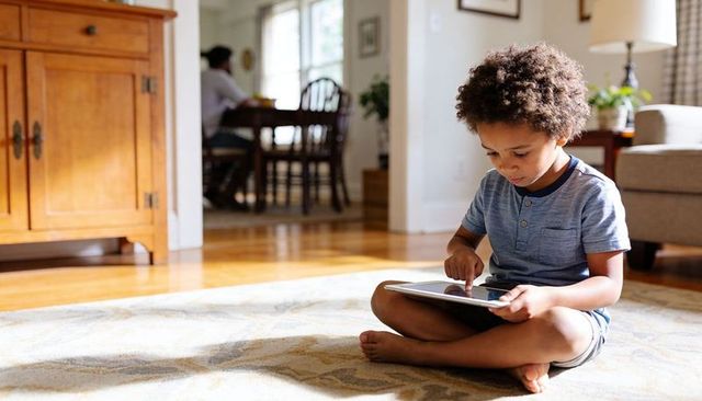 Child sitting on rug using tablet in sunlit living room, family technology moment