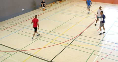 Basketball players warming up walking on indoor hardwood court with colorful lines