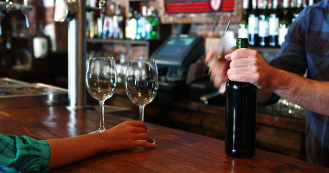 Barman opening wine bottle with corkscrew at bar counter in pub
