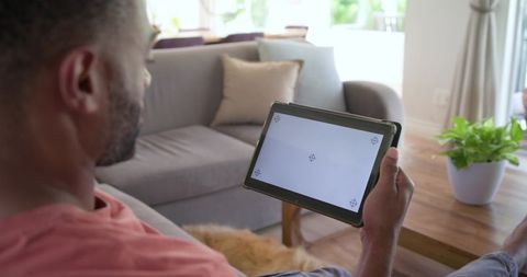 Mature man relaxing on sofa holding tablet with blank screen in modern living room