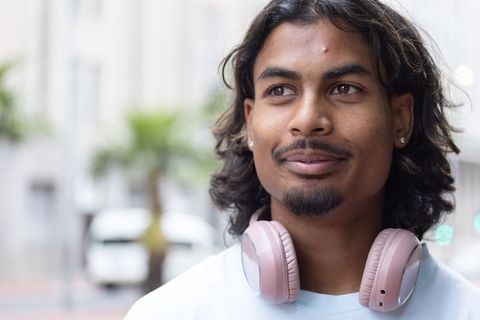 Contemplative african american man wearing pink headphones, stud earrings, urban portrait