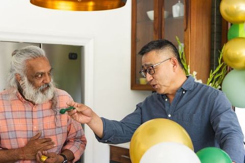 Senior asian men exchanging small gifts and chatting in kitchen with balloons