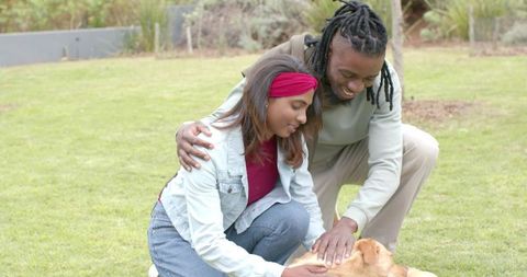 Interracial couple petting golden retriever on lawn showing affection and outdoor relaxation