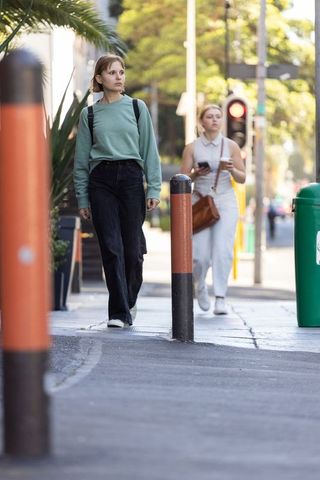 Two women walking on city sidewalk past bollards, casual street style, daytime urban lifestyle