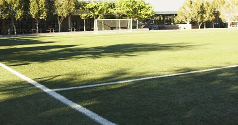 Sunlight casting long tree shadows across empty campus soccer field featuring goal and white lines