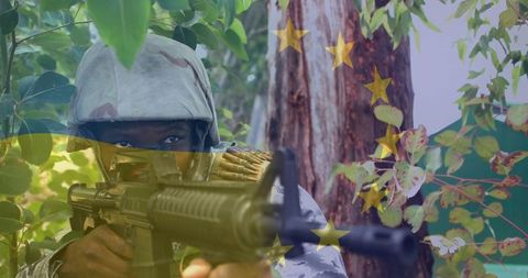 Hooded soldier aiming assault rifle in forest camouflage with golden stars overlay