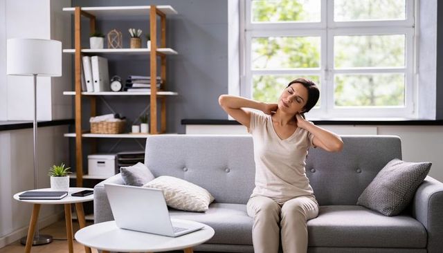 Asian woman massaging neck on sofa after remote work with laptop in bright modern living room