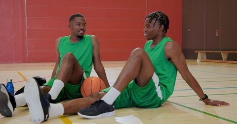 African american basketball teammates resting and talking on indoor court after practice
