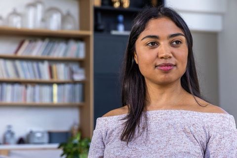 African american woman sitting in living room with bookshelf, contemplative and focused