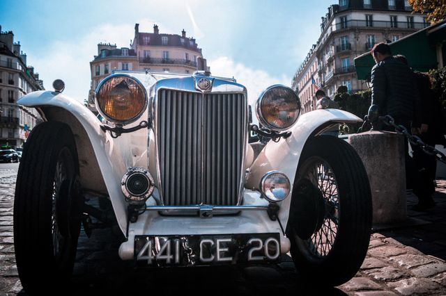 This image of a vintage white roadster provides a nostalgic glimpse into automotive history. Ideal for automotive magazines, vintage car enthusiast blogs, or travel websites showcasing European charm and historical streetscapes.