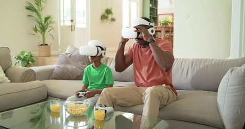 African American Father and Son Playing VR Games Together on Modern Living Room Sofa