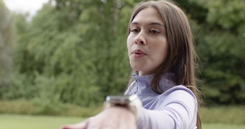 Young woman reaching forward wearing smartwatch and lavender activewear outdoor portrait in park