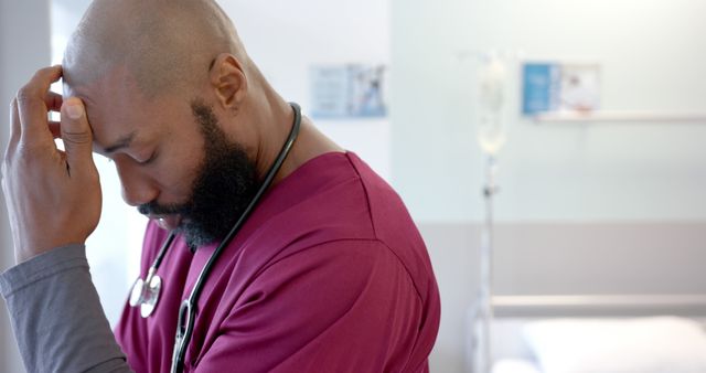 Sad african american male doctor wearing scrubs and stethoscope in hospital room. Medicine, healthcare, work and hospital, unaltered.