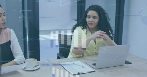 Businesswomen Reviewing Data and Documents in Modern Boardroom with Laptop and Reports