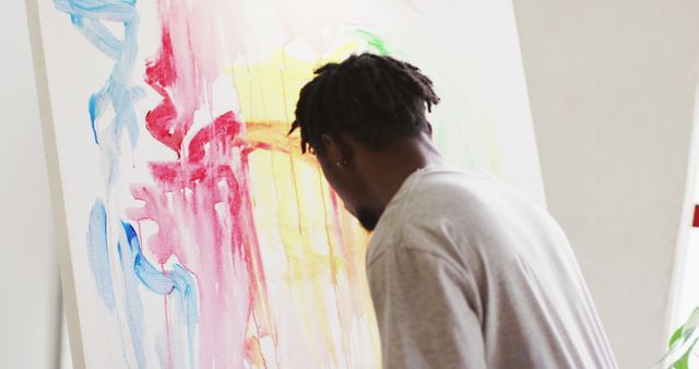 Thoughtful african american male artist sitting looking at his painting at art studio. art, hobby and creative occupation concept