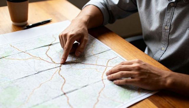 Man pointing at road map planning road trip on wooden table with coffee and pen