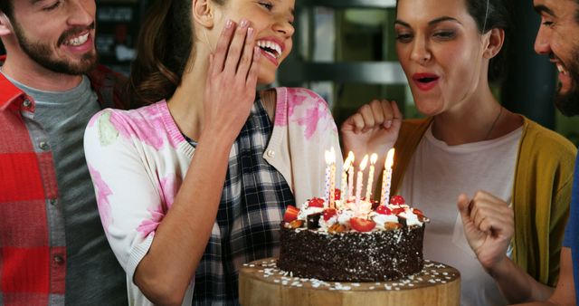 A group of diverse young adults celebrates a birthday, sharing a joyful moment around a cake with lit candles, with copy space. Smiles and laughter suggest a close-knit friendship and the excitement of a special occasion.