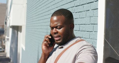 African American man talking on phone while standing by blue brick wall