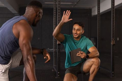 Male trainer and client celebrating progress in gym with tablet