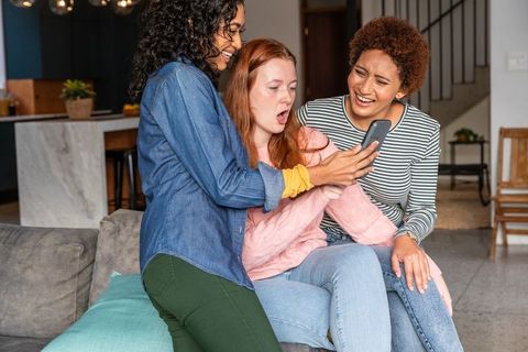 Diverse Friends Laughing at Smartphone Together in Living Room
