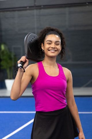 African american woman smiling holding pickleball paddle on blue court wearing magenta top