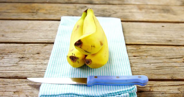 A bunch of ripe bananas is placed next to a knife on a blue-striped cloth, with copy space. Bananas are a nutritious snack, and this setup suggests preparation for a healthy meal or snack.