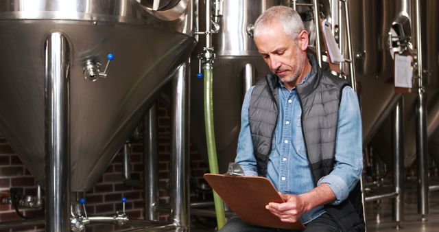 Mature brewer examining stainless steel fermentation tanks in a modern brewery. Ideal for content related to the brewing industry, quality control in brewing, professional brewers, brewery operations, and industrial processes in beverage production. Can be used in articles and marketing for breweries, brewing equipment manufacturers, and educational material on brewing.