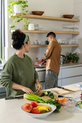 Couple chopping vegetables at sunlit kitchen island with fruit bowl and containers