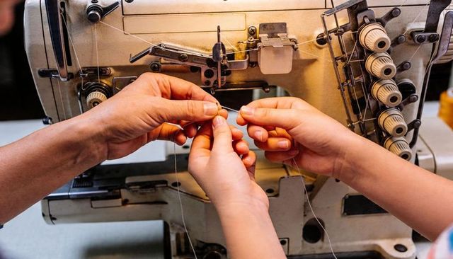 Close-up hands threading overlock machine needle, collaborative sewing workshop technique