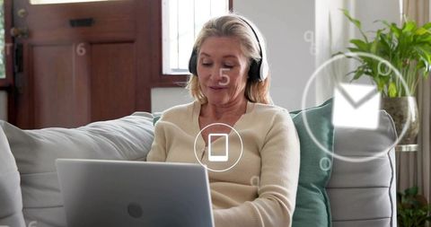 Senior woman working remotely on laptop with headphones and email notifications at home