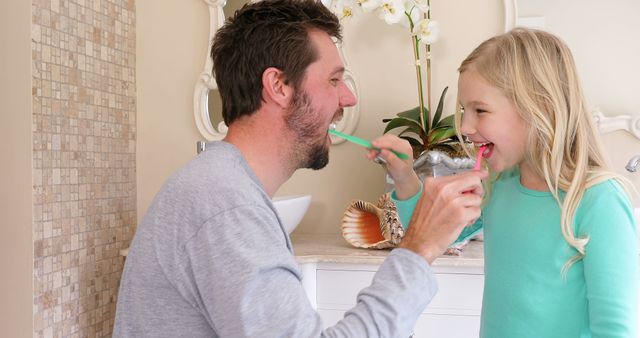 Father and daughter brushing teeth together, representing a warm and encouraging family bonding moment. Perfect for use in advertisements for dental hygiene products, family health care promotions, or articles about daily family routines and parenting tips.
