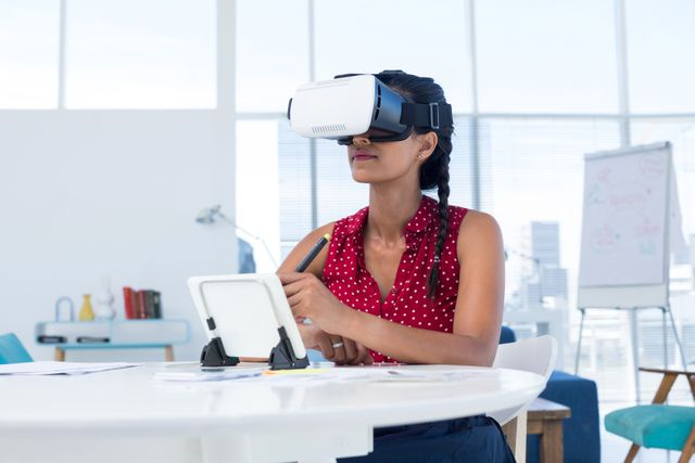 Female graphic designer in virtual reality headset using digital tablet at desk in the office