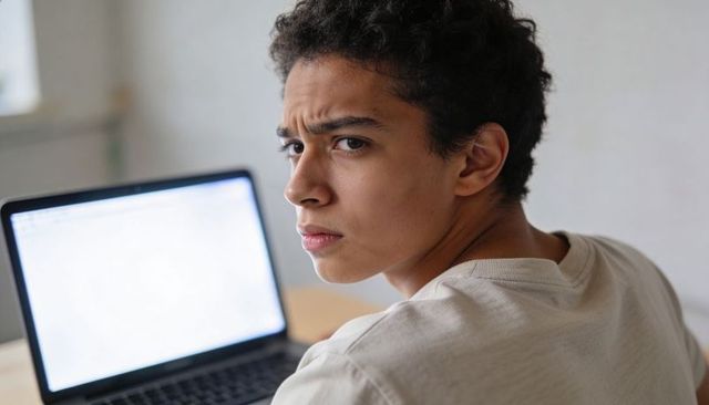 Teenager glancing over shoulder at laptop, showing skeptical look in modern home workspace