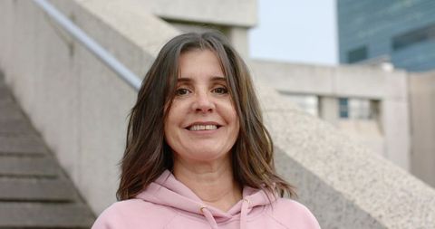Mature woman smiling in pink hoodie on concrete urban steps casual portrait for lifestyle