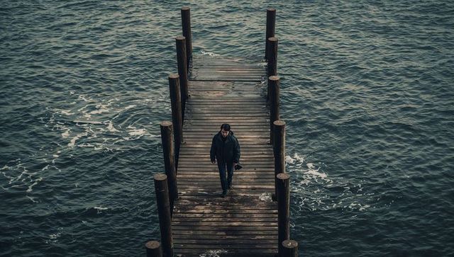 Walking photographer on weathered wooden pier over moody choppy sea lone traveler carrying camera
