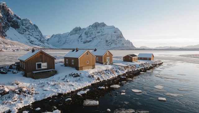 Wooden cabins nestling along snowy fjord under soft morning light with ice floes drifting