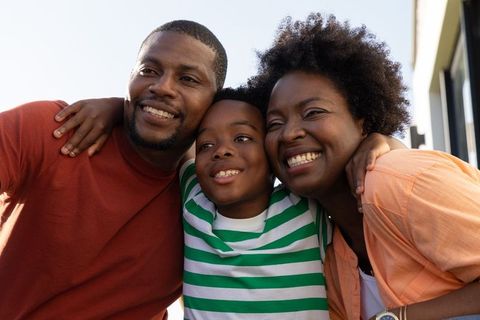 Smiling african american family hugging on porch during sunlit outdoor portrait