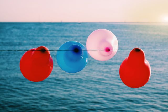 Colorful balloons are hanging on a string against the backdrop of calm ocean water. The sunset in the distance adds a warm hue to the scene, making it perfect for themes of celebration, tranquility, or beach parties. Great for use in summer event promotions, party invitations, or travel brochures.