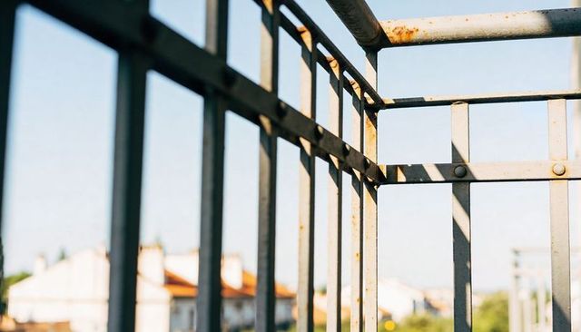Sunlit rusted balcony railing casting geometric shadows over orange tiled rooftops