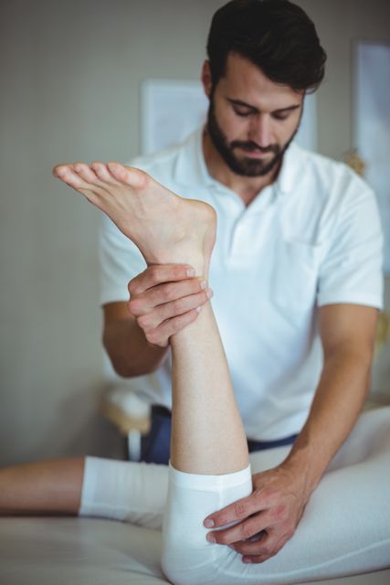 Physiotherapist treating patient's leg in a clinical setting. Ideal for use in healthcare, rehabilitation, and wellness content. Can be used in articles, blogs, and promotional materials related to physical therapy, injury recovery, and medical treatments.
