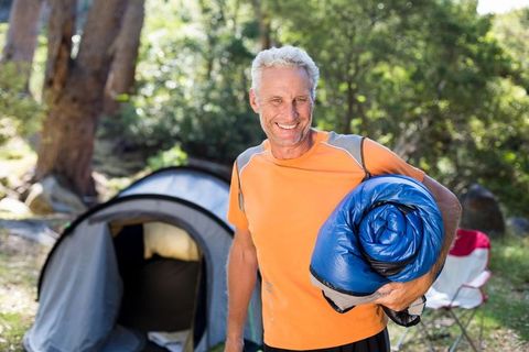 Happy camper holding sleeping bag in forest campsite