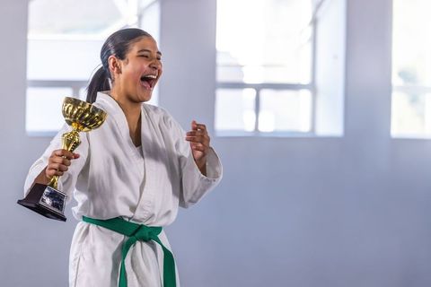 Teen martial artist celebrating victory with trophy in dojo white gi green belt