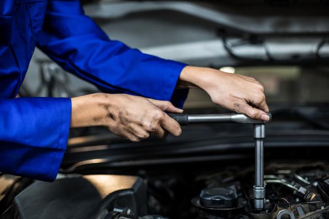 Hands of female mechanic servicing a car in repair garage